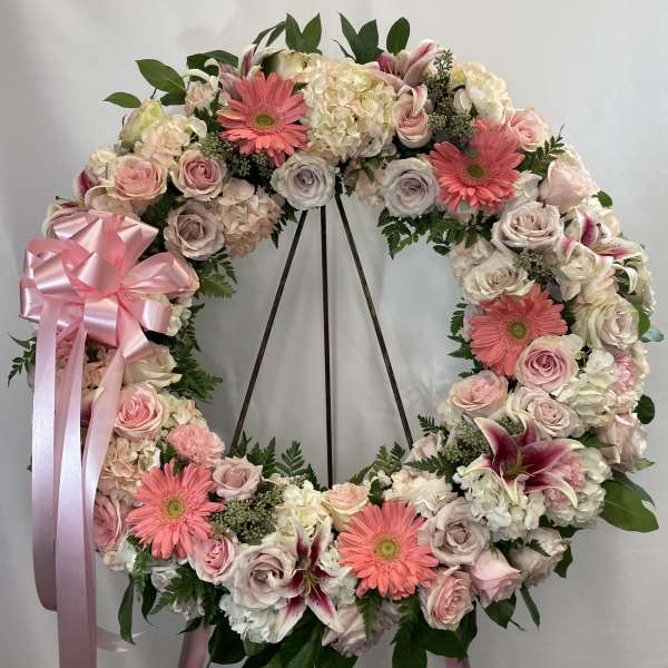 Large pink and white floral wreath on a stand with ribbon bow