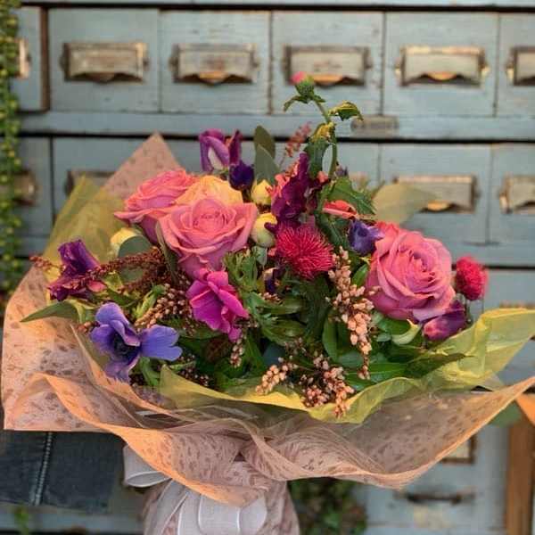 Bouquet of pink roses and purple flowers wrapped in pale paper