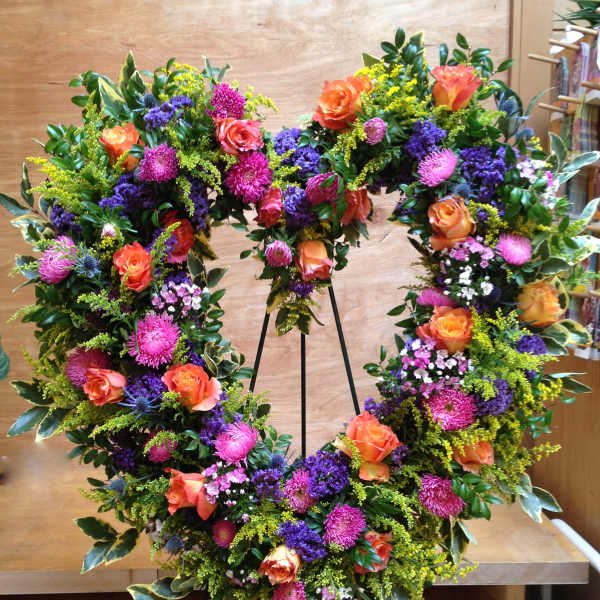 Large floral wreath with orange roses, pink blooms, and purple accents