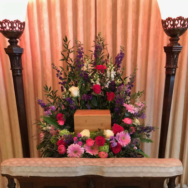 Large funeral floral arrangement with roses and daisies around a wooden urn