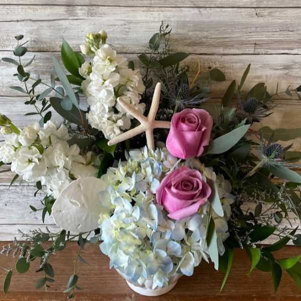 Pink roses and white flowers arranged with a starfish in a white vase