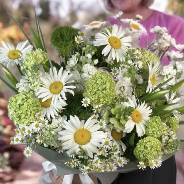 Bouquet of white daisies and green pom-pom flowers wrapped in gray paper