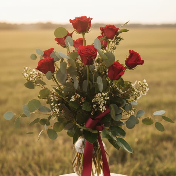 Red roses in a glass vase with greenery and a burgundy ribbon