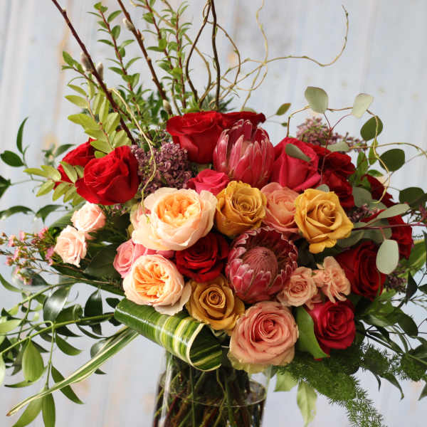 Mixed bouquet of red, peach, and yellow roses with greenery in a glass vase