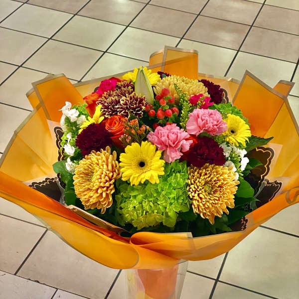 Colorful mixed bouquet in orange wrap with a tall clear vase