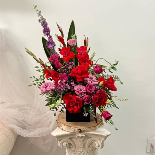 Tall arrangement of red and pink flowers in a black container