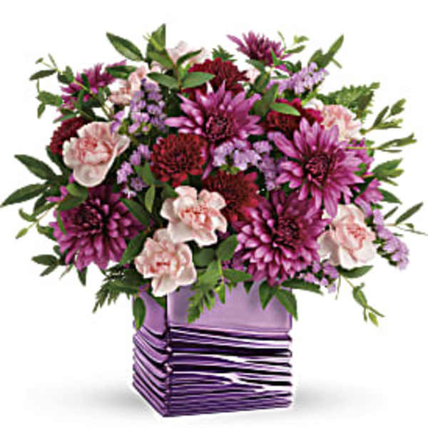 Purple and pink mixed flower arrangement in a square lavender vase