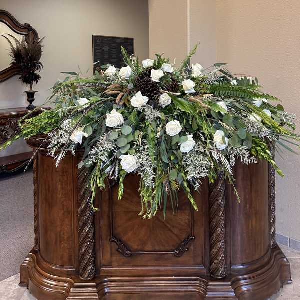 Large white rose arrangement draped over a wooden casket