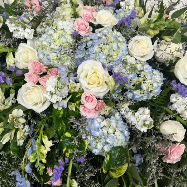Large mixed floral arrangement with white roses, blue hydrangeas, and pink spray roses