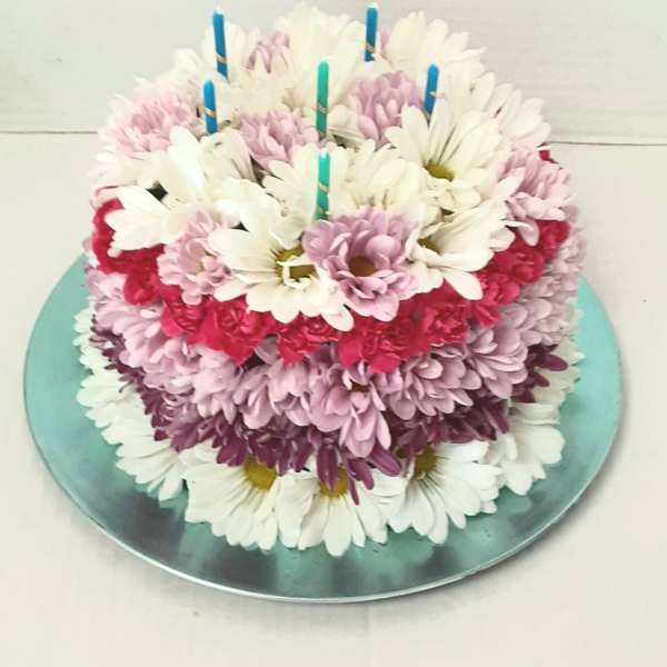 Round cake covered with white, pink, and purple daisies and candles on top