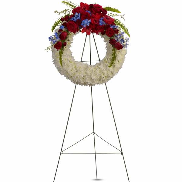 Standing funeral wreath with red roses, white flowers, and blue accents on an easel