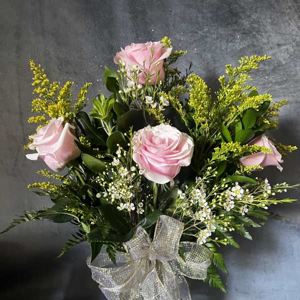 Pink roses in a glass vase with white filler flowers and a sheer ribbon