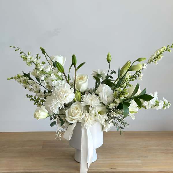 White floral arrangement in a white vase with long stems and ribbon