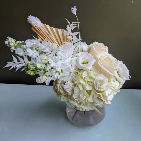 White floral arrangement in a round glass vase with roses and hydrangeas