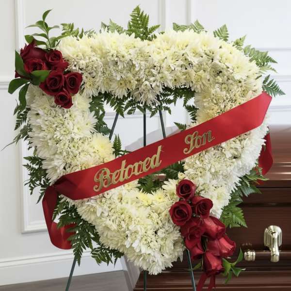 Heart-shaped white floral funeral wreath with red roses and a red memorial ribbon