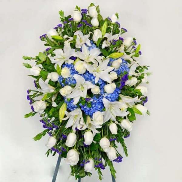 Standing floral spray with white lilies, blue hydrangeas, and purple accents