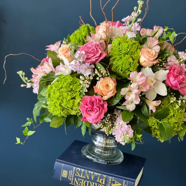 Pink and peach roses arranged with green hydrangeas in a glass vase.