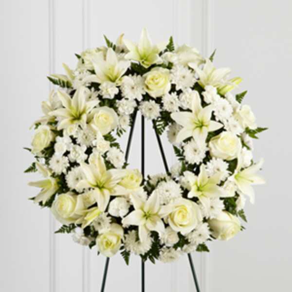 White floral wreath on a black stand with roses and lilies