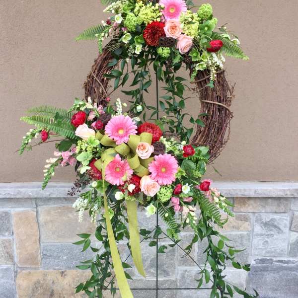 Floral wreath with pink gerberas, roses, and greenery on a grapevine frame