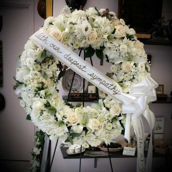 Large white sympathy wreath with a ribbon on a stand