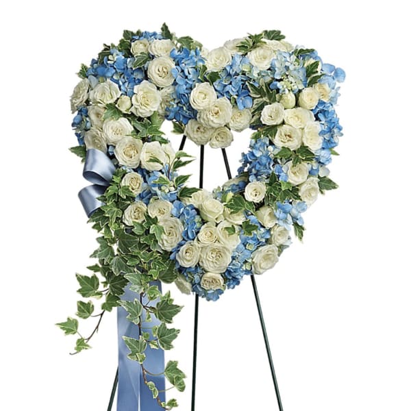 Heart-shaped floral wreath with white roses and blue hydrangeas on a stand
