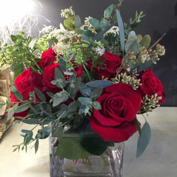 Red roses in a clear square vase with white filler flowers and eucalyptus