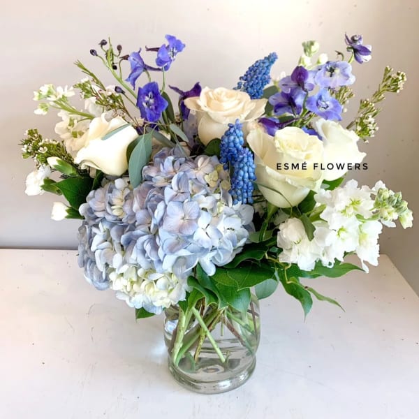 Bouquet of white roses, blue hydrangeas, and purple flowers in a glass vase