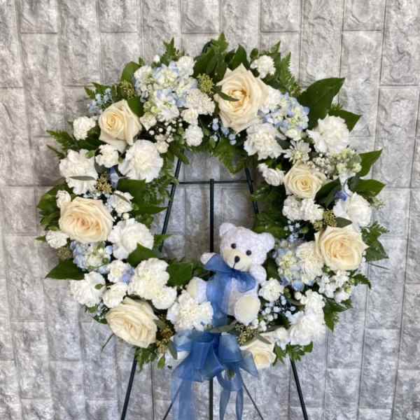 Heart-shaped floral wreath with cream roses, white flowers, and a blue ribbon on an easel