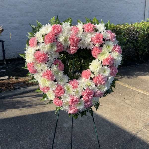 Heart-shaped floral wreath of pink and white flowers on a stand