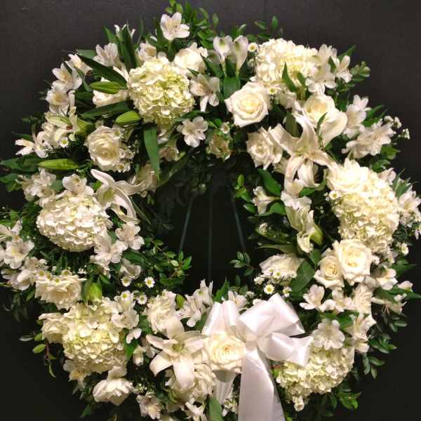 White floral wreath with a satin ribbon bow on a dark background