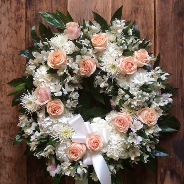 Round floral wreath with peach roses and white flowers on a wooden background