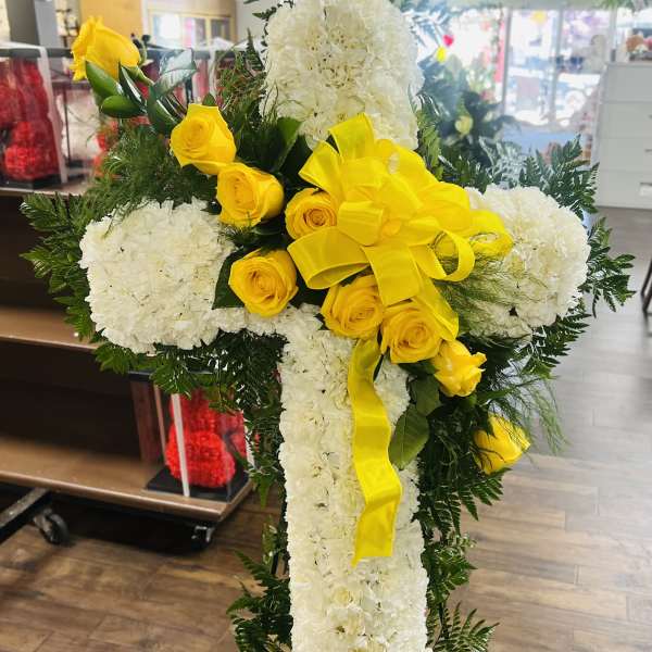 Standing floral cross with white blooms and yellow roses on an easel