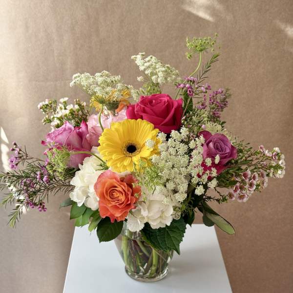 Mixed bouquet of roses, hydrangeas, and a yellow gerbera daisy in a glass vase