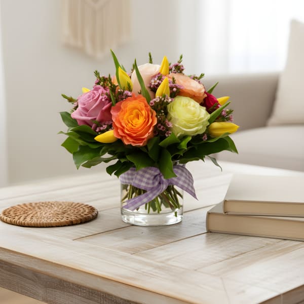 Colorful bouquet of roses and tulips in a glass vase with a purple ribbon