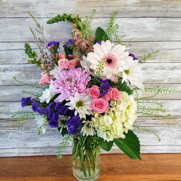 Mixed bouquet of pink, white, and purple flowers in a clear glass vase
