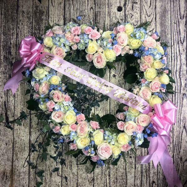 Heart-shaped floral wreath with pink and yellow roses and a pink ribbon