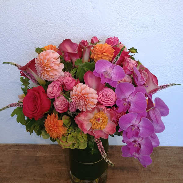 Colorful bouquet of roses, dahlias, calla lilies, and orchids in a glass vase
