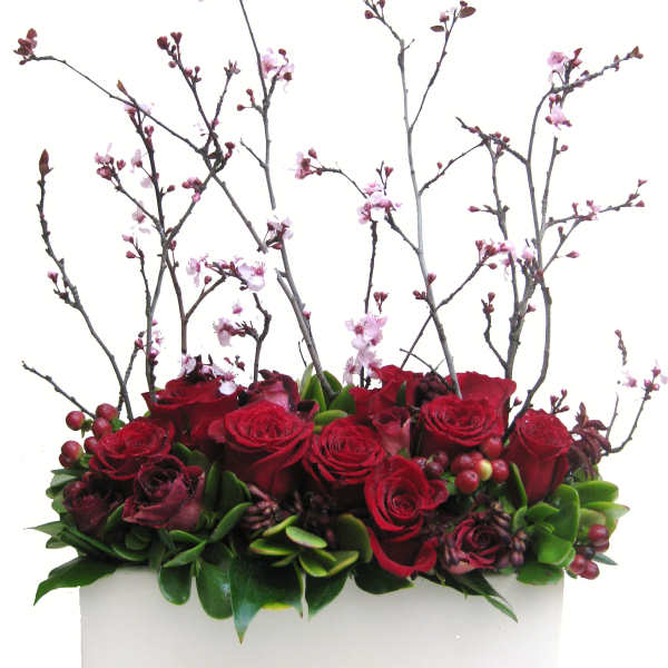 Red roses and pink blossoms arranged in a white rectangular container