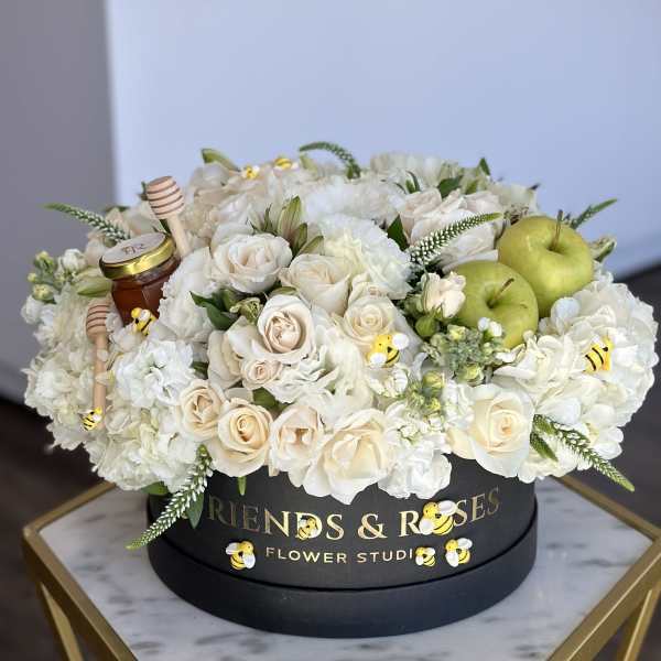White roses and hydrangeas in a black hat box with green apples and honey jars