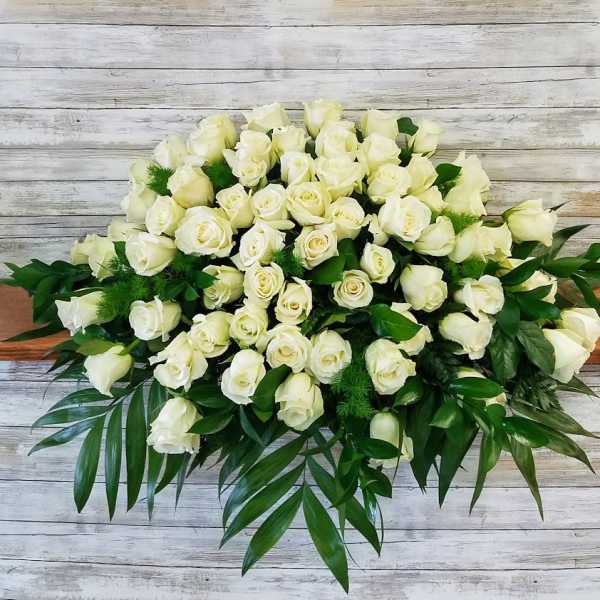 Large bouquet of white roses with green foliage on a wooden surface
