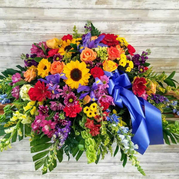 Colorful casket spray with sunflowers, roses, and a blue ribbon