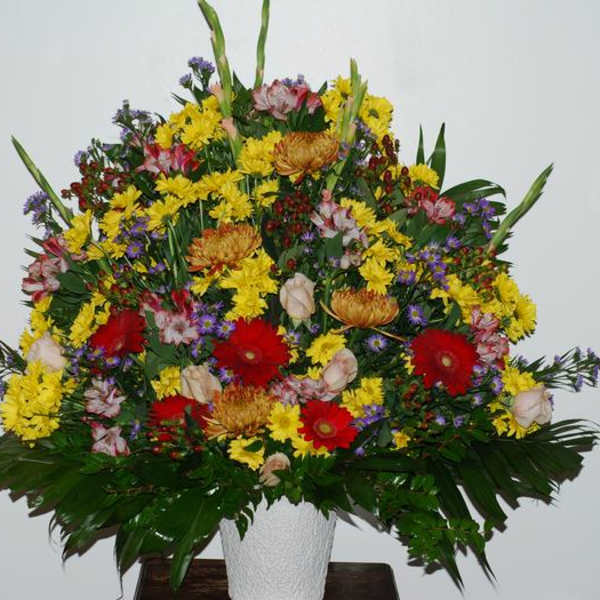 Large mixed flower arrangement in a white vase with red, yellow, and purple blooms