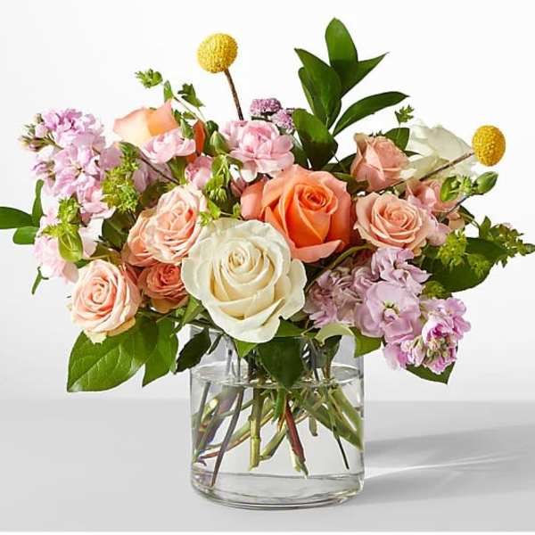 Peach, pink, and white roses with accent flowers arranged in a clear glass vase
