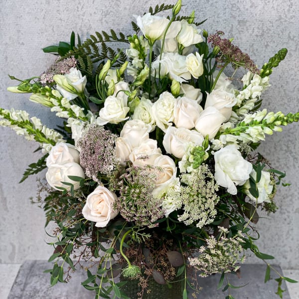 White roses and snapdragons in a dark vase with trailing greenery