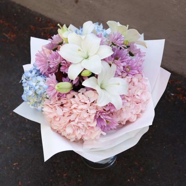 Bouquet of white lilies, pink chrysanthemums, and blue hydrangeas in white wrap