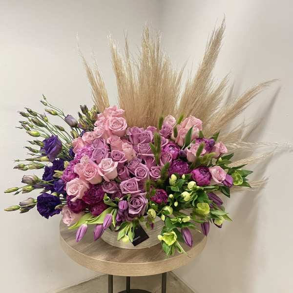 Large pink and purple rose arrangement with tulips and pampas grass in a low round container