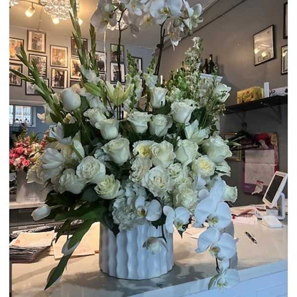 Large white floral arrangement in a white vase with orchids and roses
