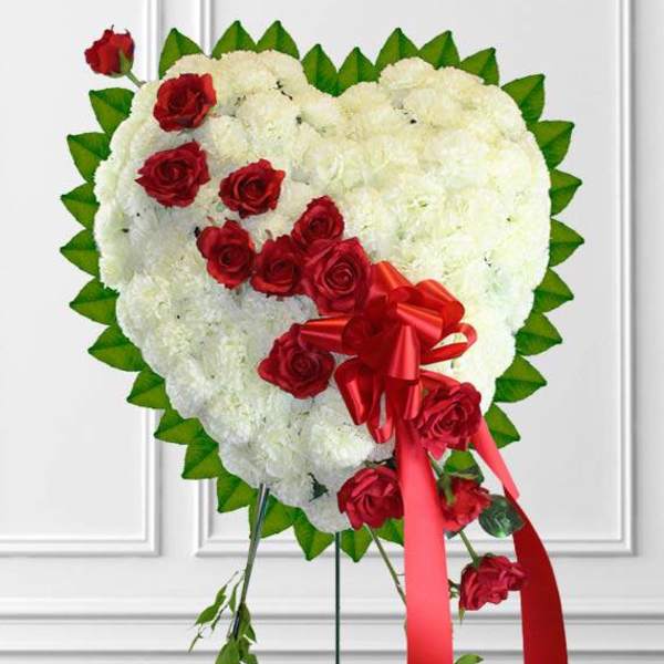Heart-shaped white floral arrangement with red roses and a red ribbon