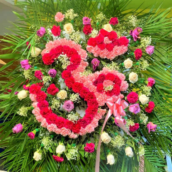 Heart-shaped floral wreath with pink and red flowers and a ribbon bow