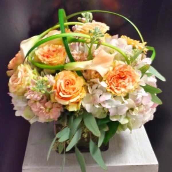 Peach and white floral arrangement in a dark container with looping green accents